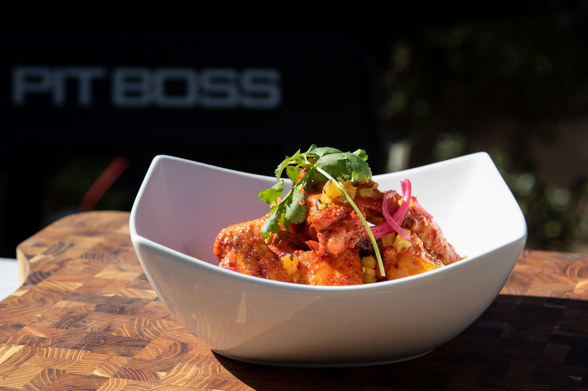 seasoned wings with a parsley garnish in white bowl on top of wooden cutting board in front on Pit Boss Pellet Grill