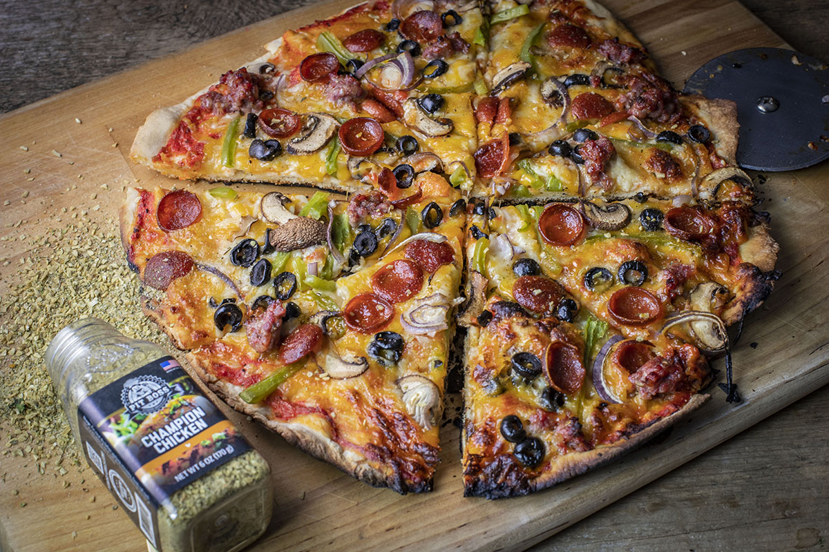 whole cooked pizza on wooden board next to bottle of pit boss seasoning