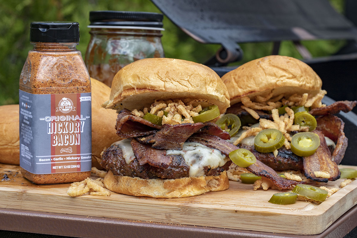 Burgers with onions and bacon next to a bottle of hickory bacon rub