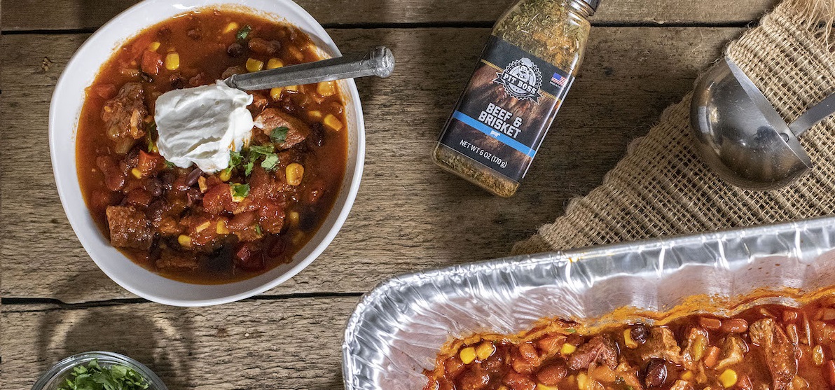 delicious looking Smoked Brisket chili with sour cream served in a bowl next to pit boss beef and brisket rub on wooden table